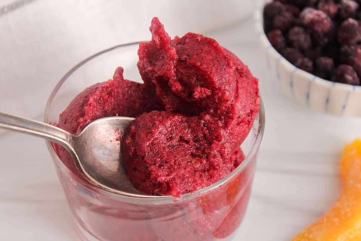 A spoon taking some blueberry peach sorbet from a bowl.