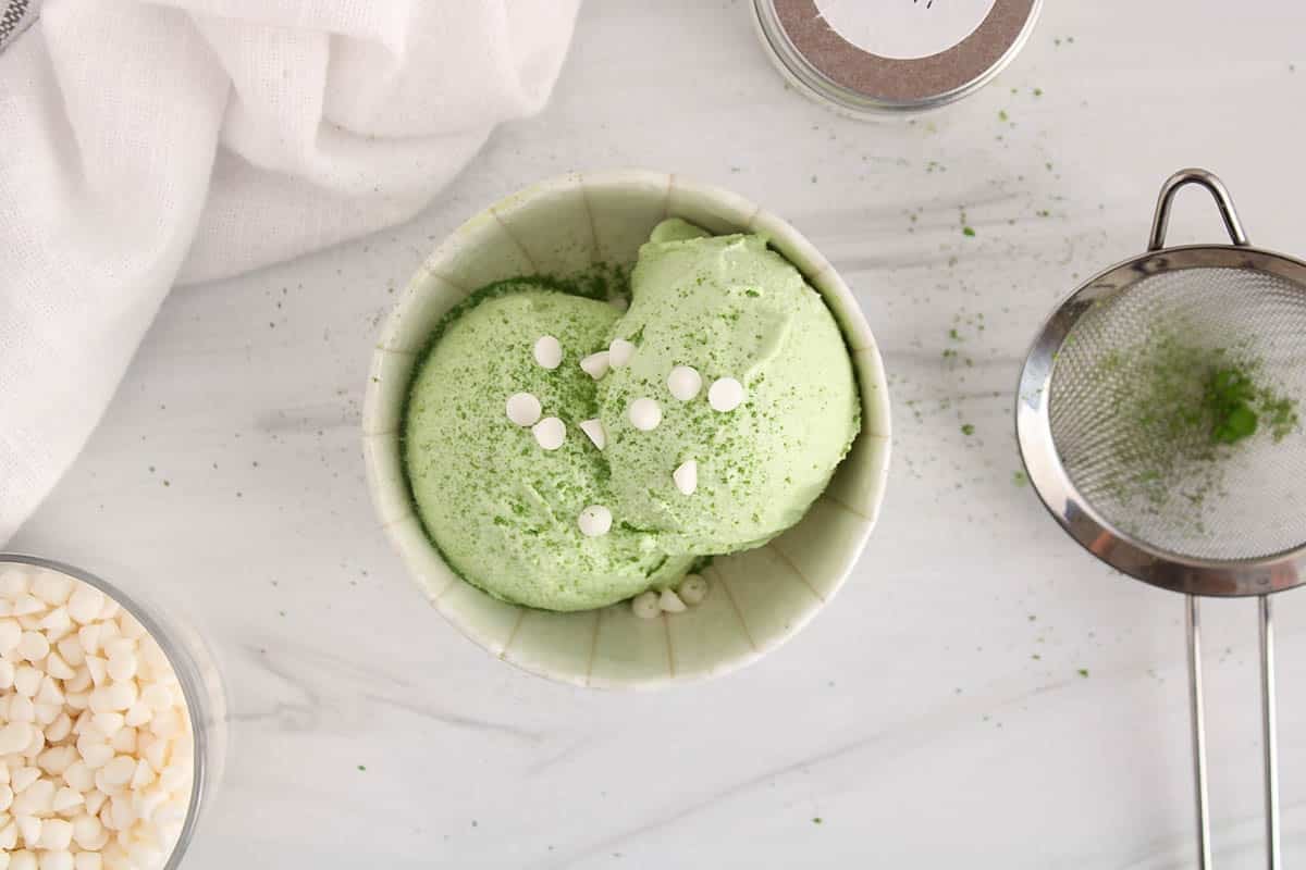 A bowl of vegan coconut matcha ice cream topped with white chocolate chips.