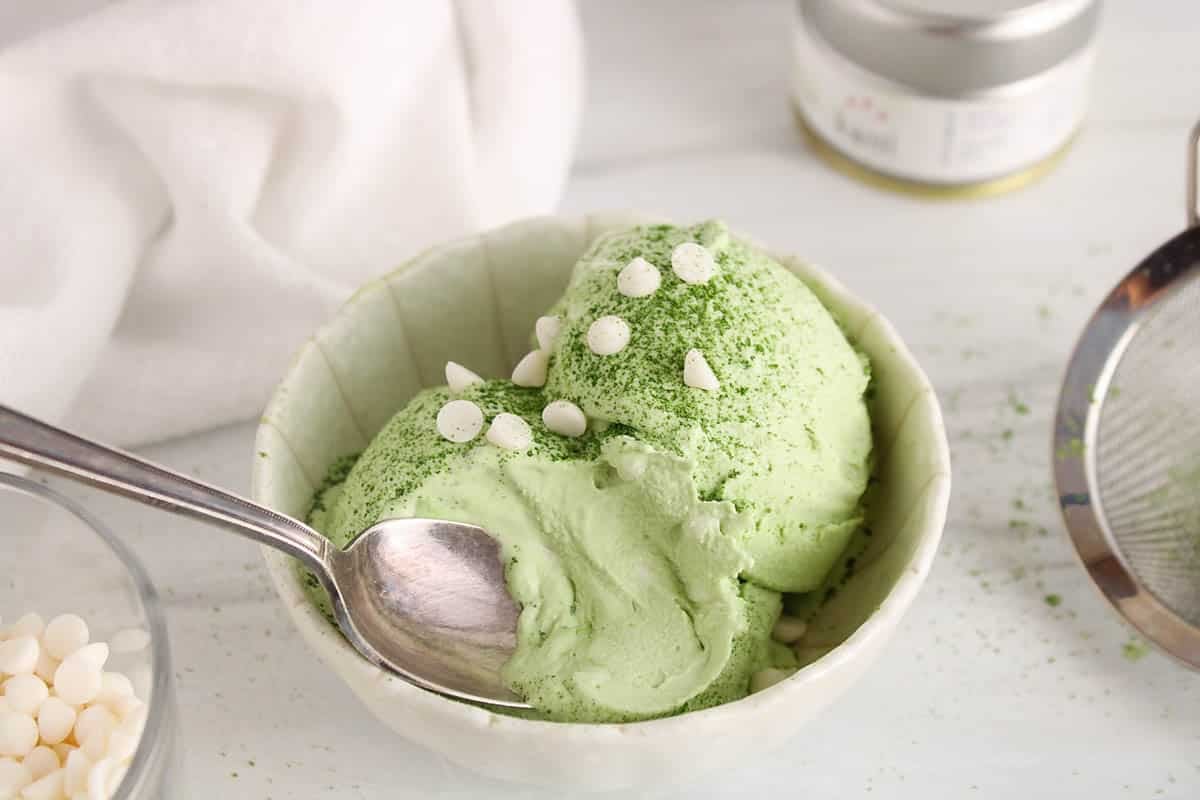 A spoon taking a bite of vegan coconut matcha ice cream from a bowl.