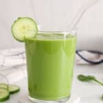 Tall glass of cucumber spinach smoothie with a straw and a slice of cucumber against the rim.