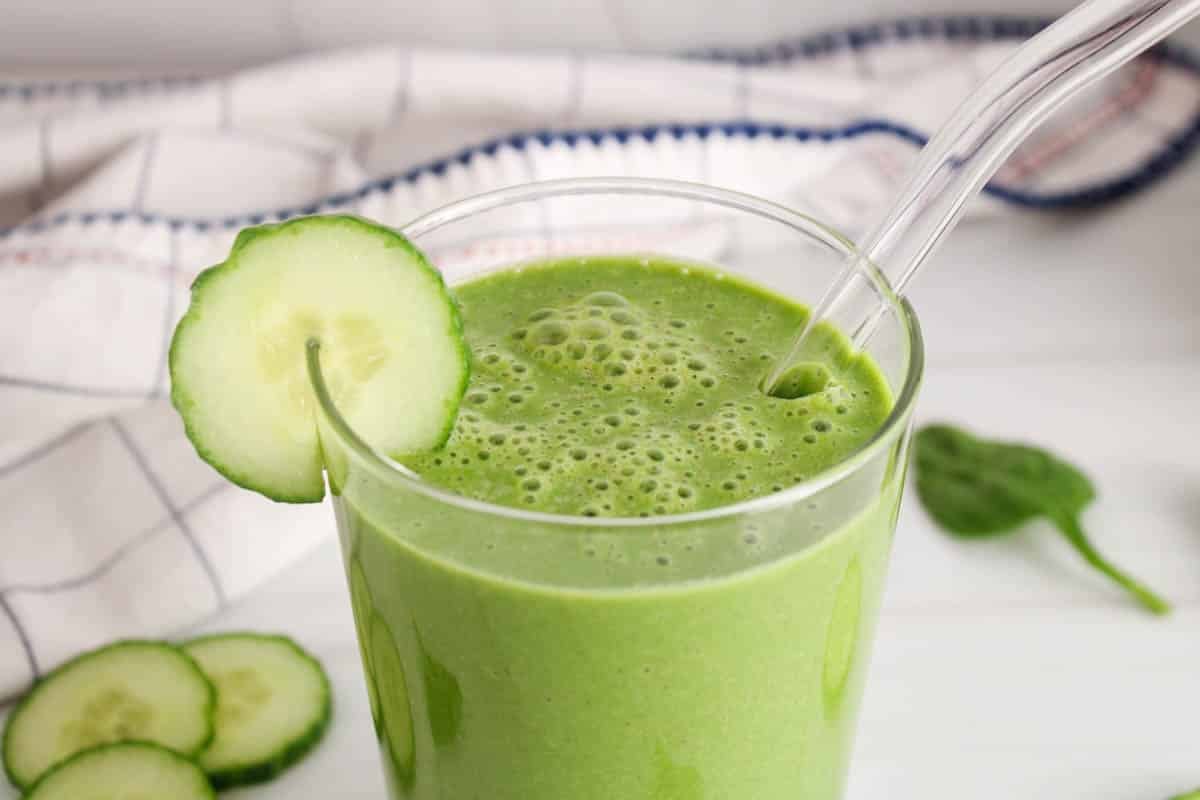 Top of a glass of cucumber smoothie with a straw and a slice of cucumber.