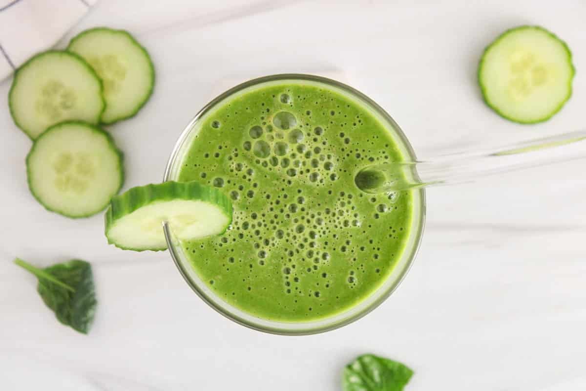 Top of a glass of cucumber smoothie with a straw and a slice of cucumber.