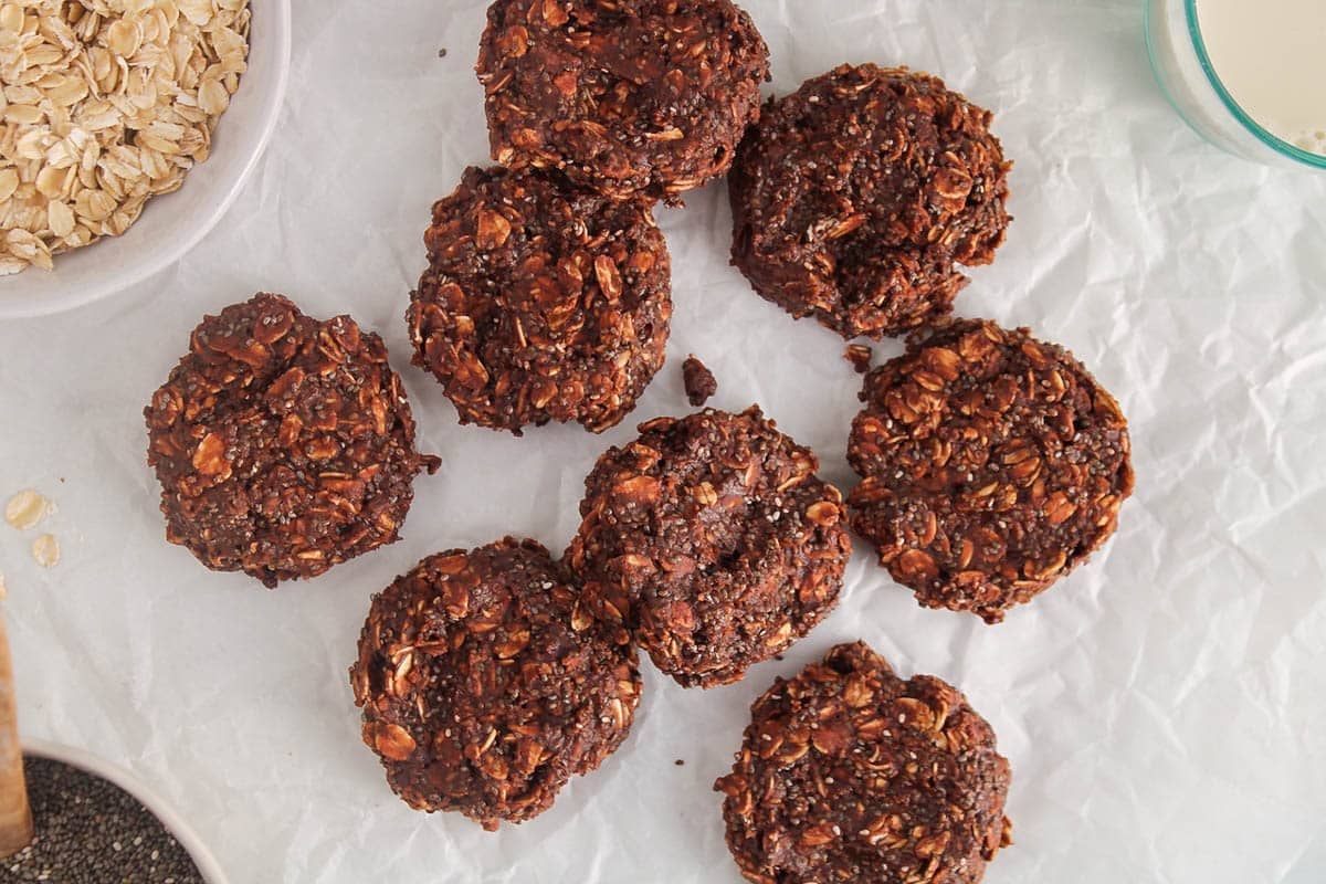 No Bake Protein Cookies on parchment paper with a side of oats and chia seeds.