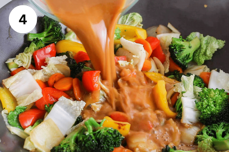 A sauce pouring in a large wok with cooking vegetables.