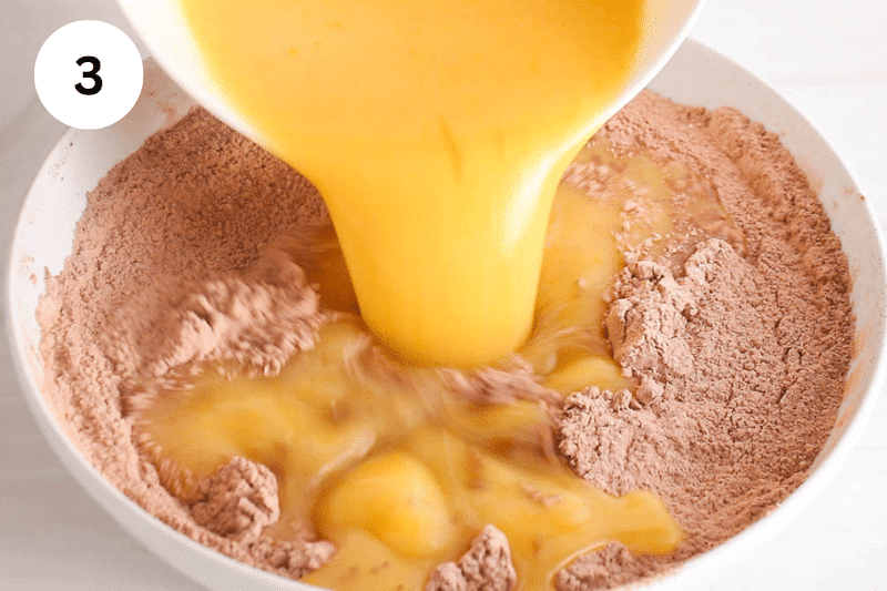 A orange mixture pouring over dry ingredients in a bowl.