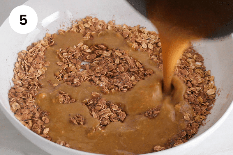 A peanut butter sauce pouring over a mixing bowl with oats and cacao powder.