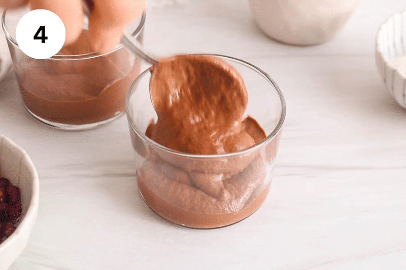 A large spoon transferring a chocolate pudding in a small container.