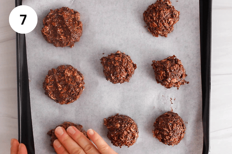 A hand pressing on balls of cookie dough on parchment paper.