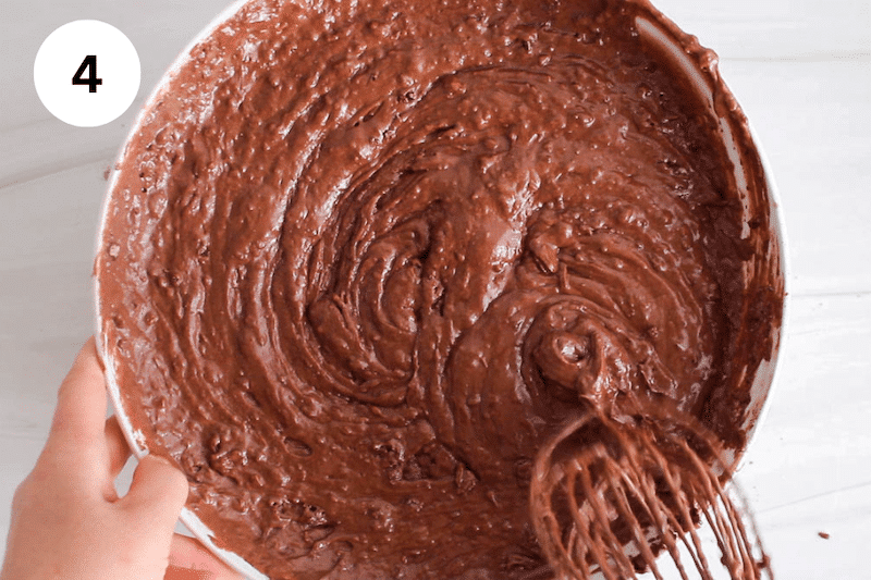 A large whisk stirring in a bowl with a chocolate cake batter.