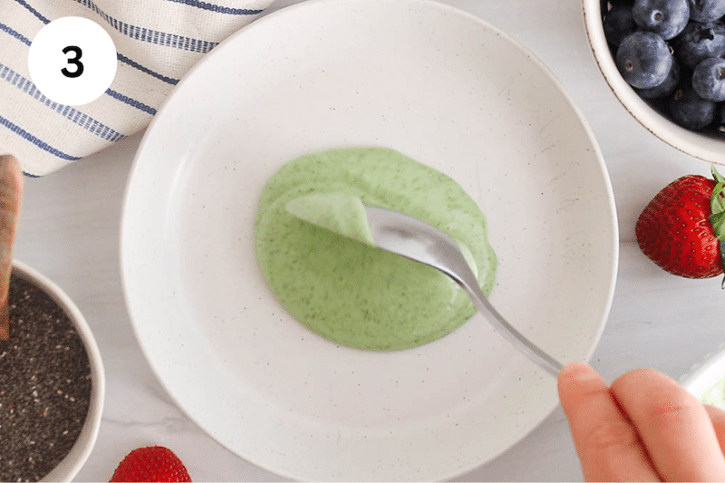 A large spoon adding matcha yogurt over a bowl.