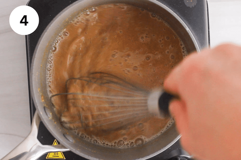 A large whisk stirring in a small pot with a peanut butter sauce.