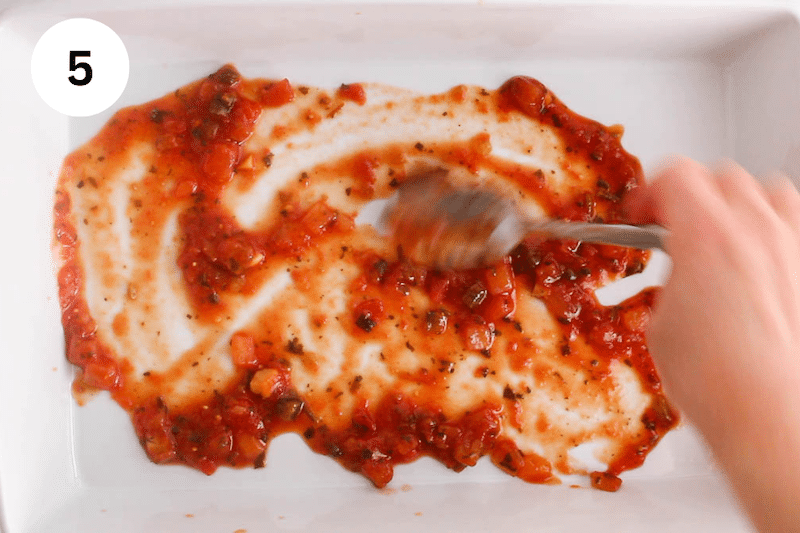 A spoon spreading some salsa to the bottom of a large baking dish.
