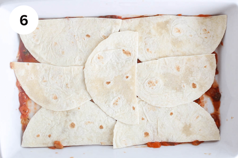 A large baking dish with tortillas spread out over salsa.