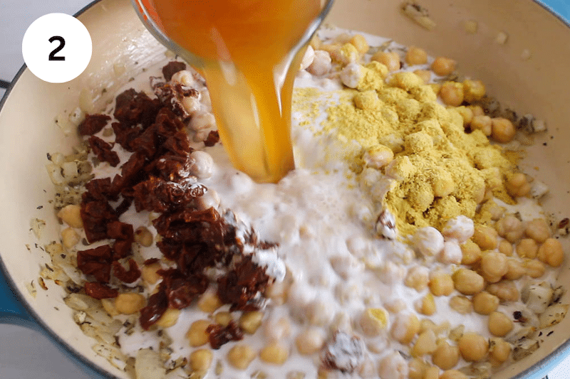 Broth pouring over a pan with chickpeas and seasonings.
