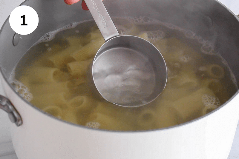 A cup taking some pasta cooking water from a large pot.