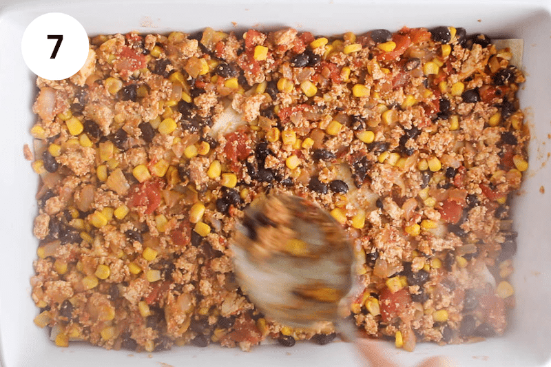 A large spoon spreading out a tofu bean mix in a large baking dish.