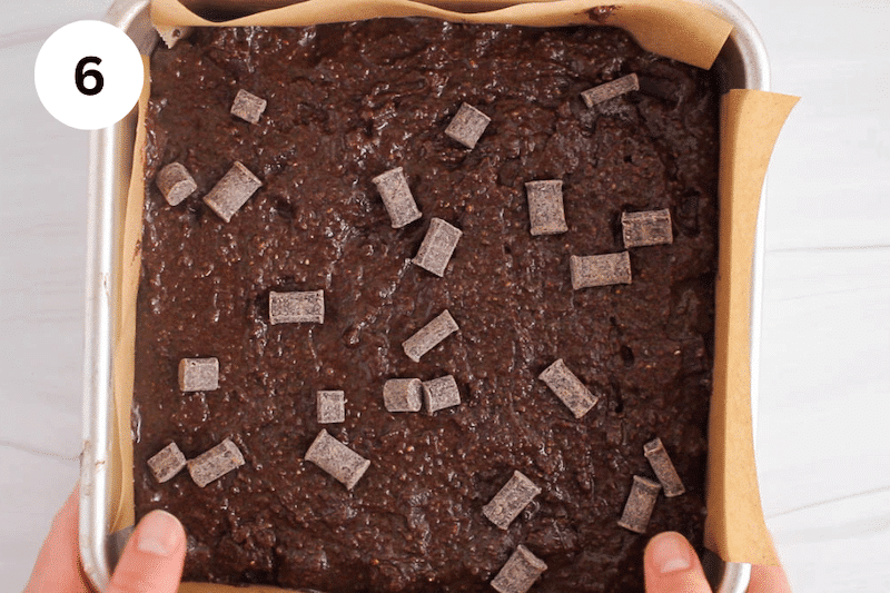 A baking pan with a brownies batter covered with chocolate chips.