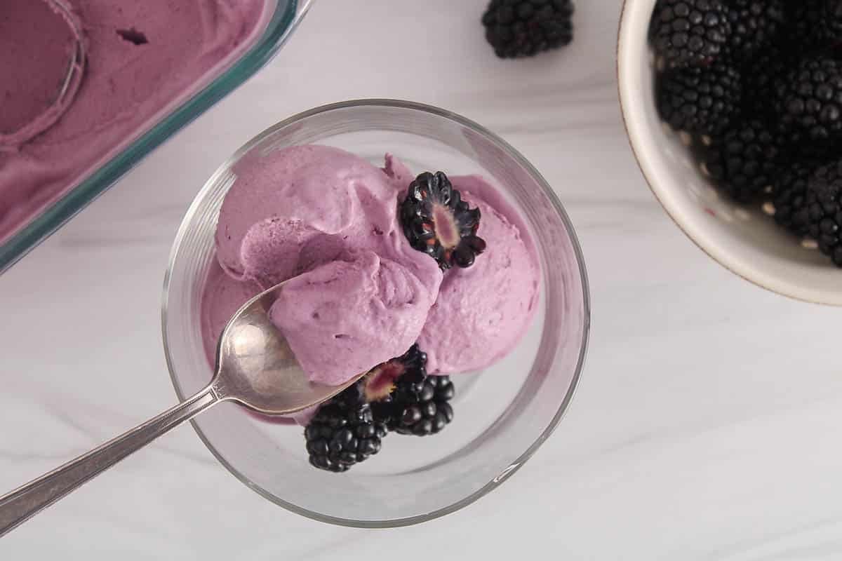 A spoon taking some vegan blackberry ice cream from a bowl.