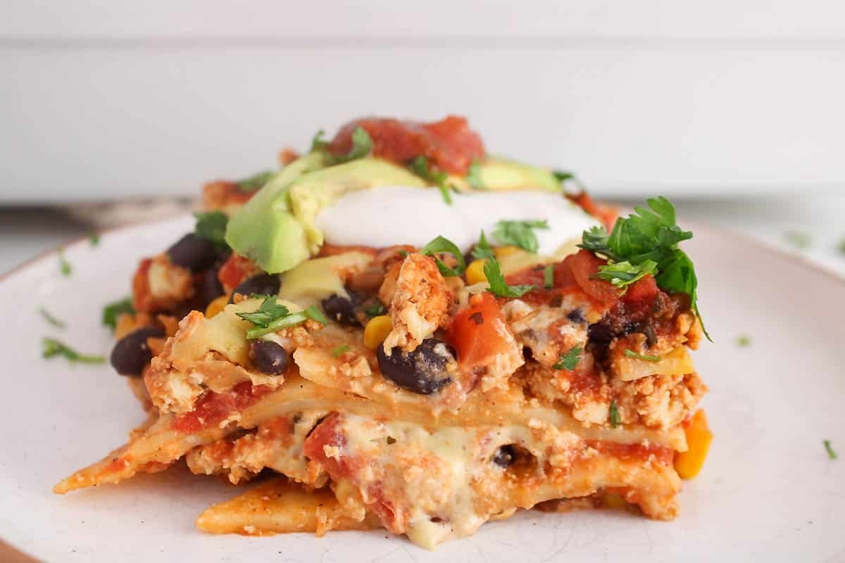 A sliced of vegan taco casserole on a plate topped with vegan sour cream and avocado.