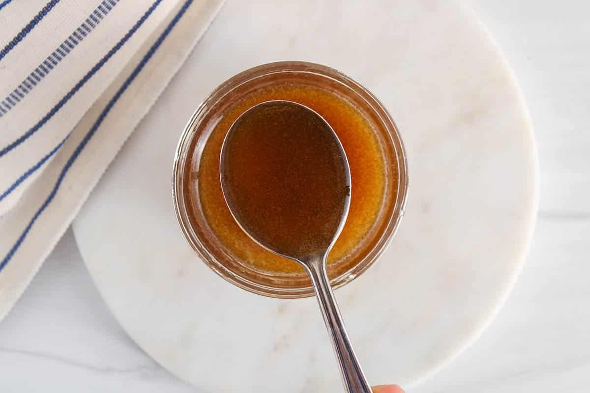 A spoon taking some olive oil caramel from a jar.