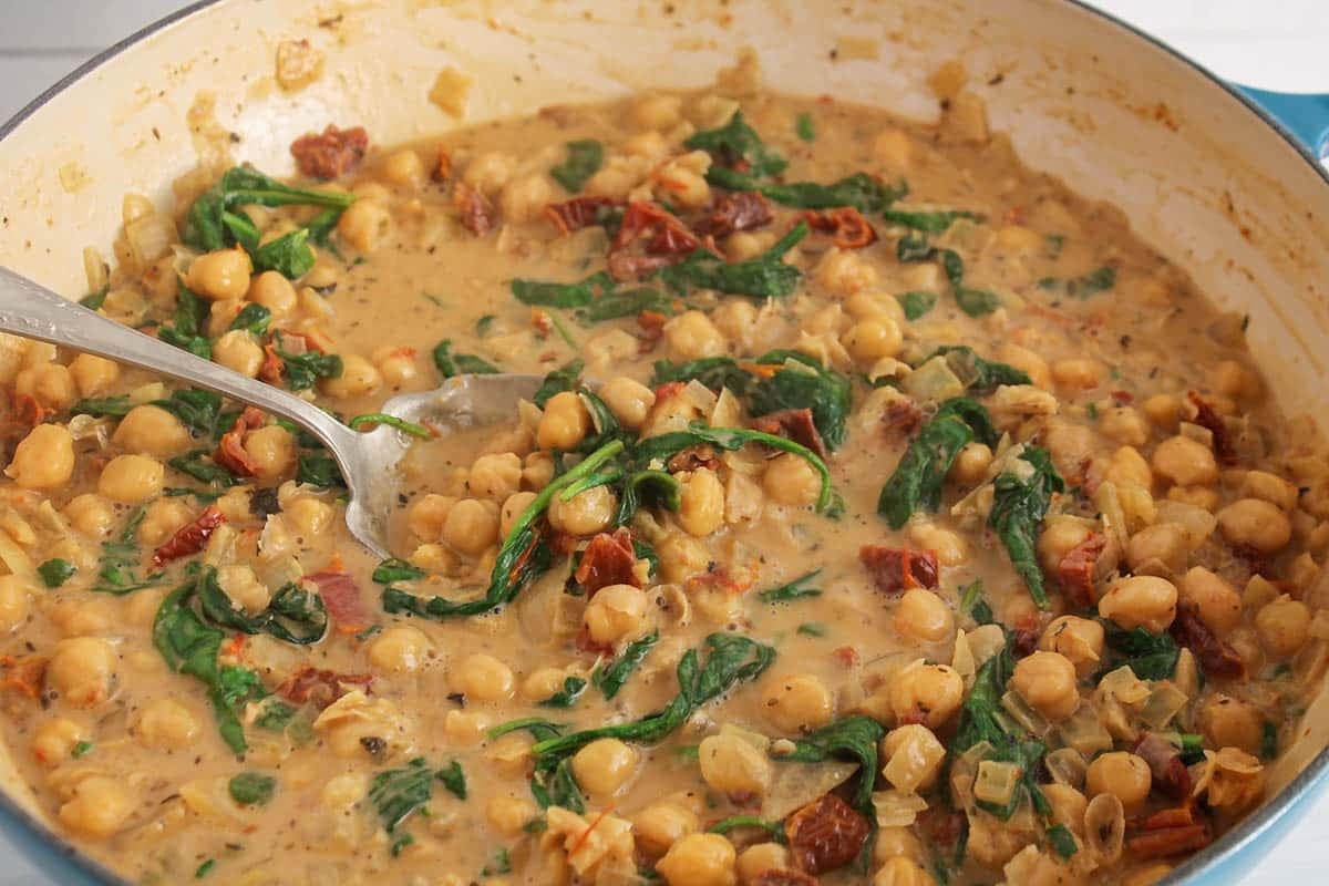 A large pan with a creamy vegan Tuscan chickpea with spinach and sun-dried tomatoes.