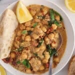 A spoon in a bowl of creamy vegan Tuscan chickpeas with a side of bread and lemon wedge.