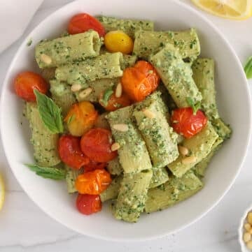 White bowl with creamy pesto rigatoni garnished with roasted tomatoes.
