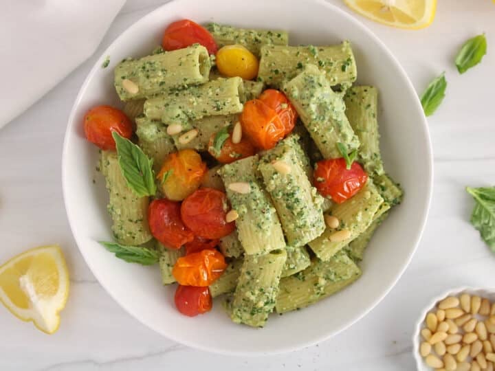 White bowl with creamy pesto rigatoni garnished with roasted tomatoes.