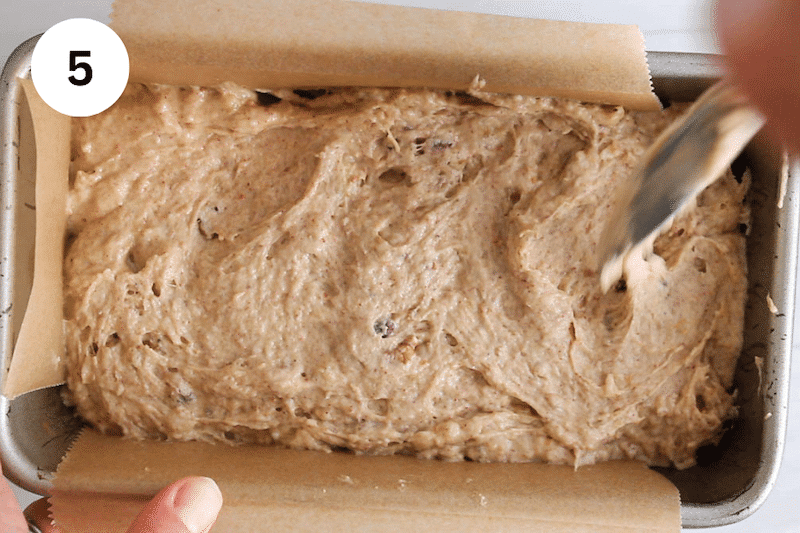 A spatula spreading banana bread batter in a loaf pan.