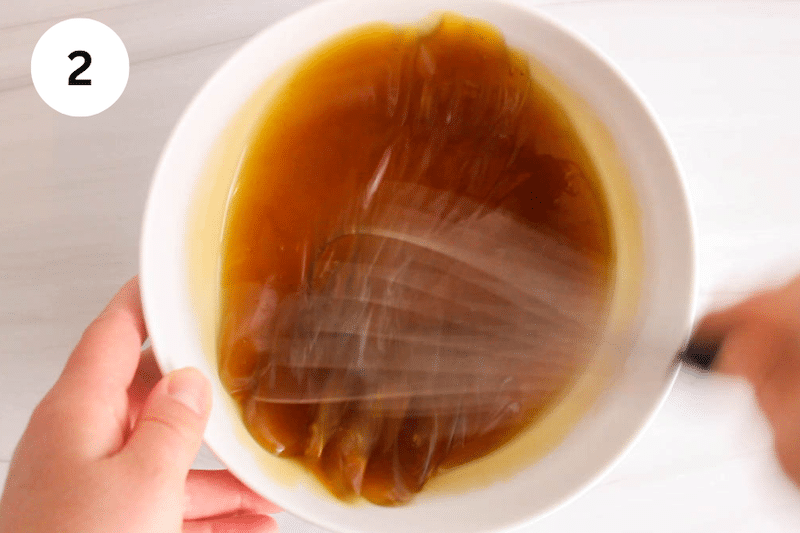 A large whisk stirring in a bowl with olive oil and maple syrup.