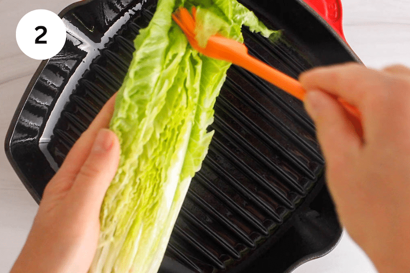 A brush brushing some olive oil over halves of Romaine.