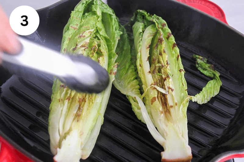 Tongs flipping some romaine over a grill.