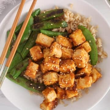 A bowl of sesame ginger tofu over rice with a side of beans.