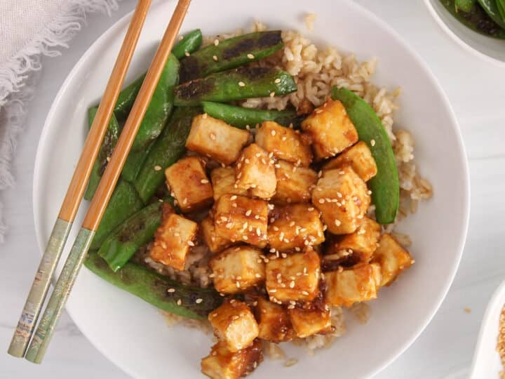 A bowl of sesame ginger tofu over rice with a side of beans.