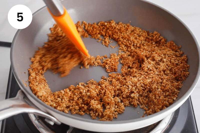 A spatula stirring in a pan with breadcrumbs.