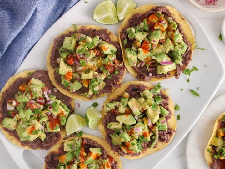 A platter of avocado tostadas with a drizzle of hot sauce.