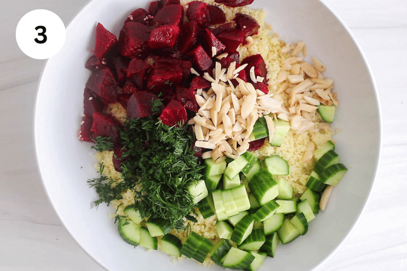 A large white bowl with couscous, beets, cucumber, dill and almonds.