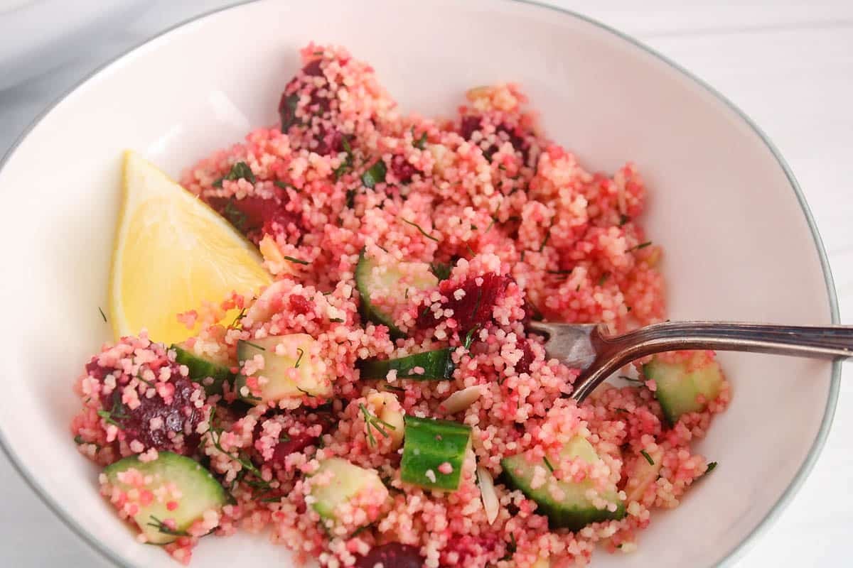 A fork in a bowl of beet couscous salad.