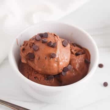White bowl with a creamy vegan chocolate ice cream filled with chocolate chips.