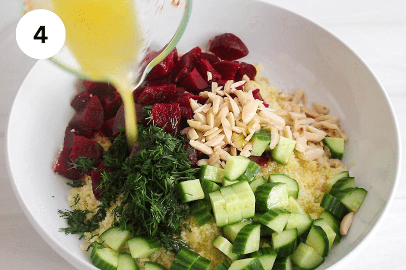 A large white bowl with a dressing pouring over couscous and vegetables.