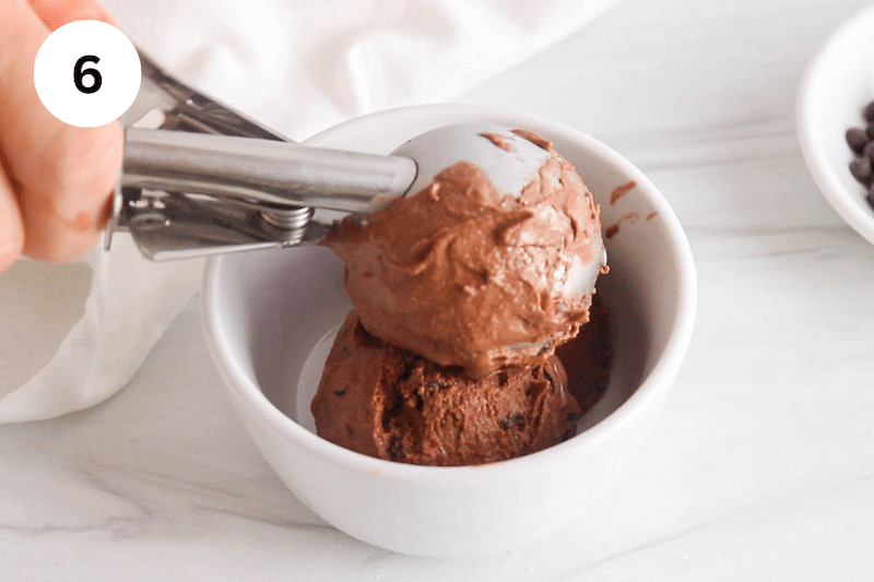 An ice cream scoop serving vegan chocolate coconut ice cream in a small bowl.
