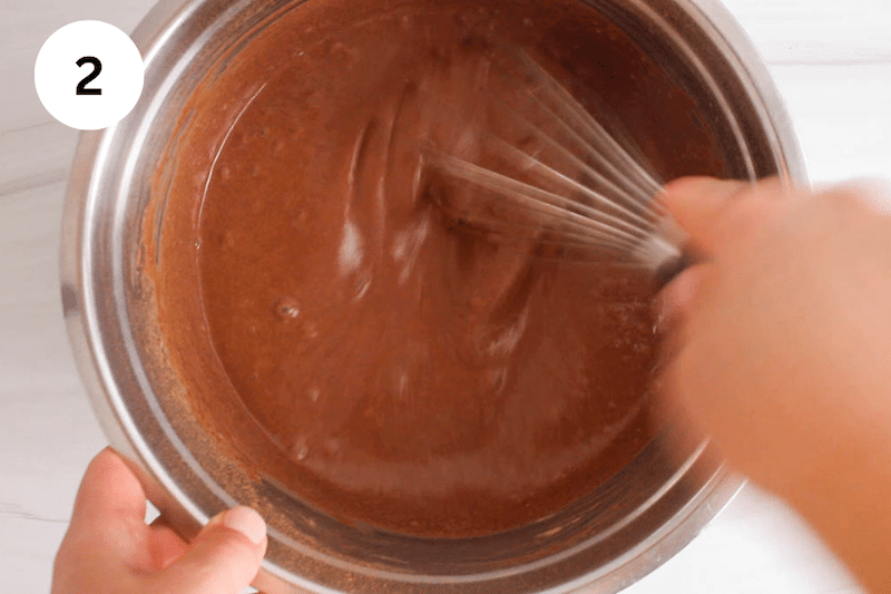 A large whisk mixing a chocolate chocolate milk mixture in a large bowl.