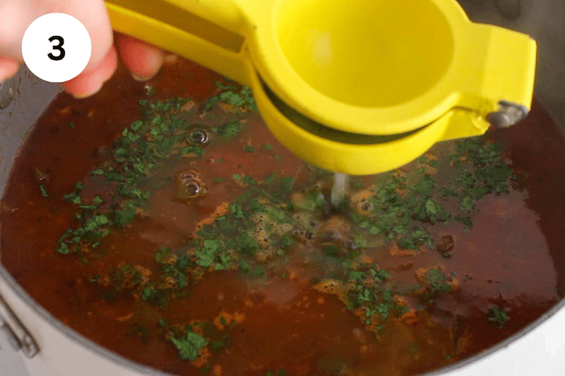 A lemon squeezer adding lime juice to a large pot of soup.