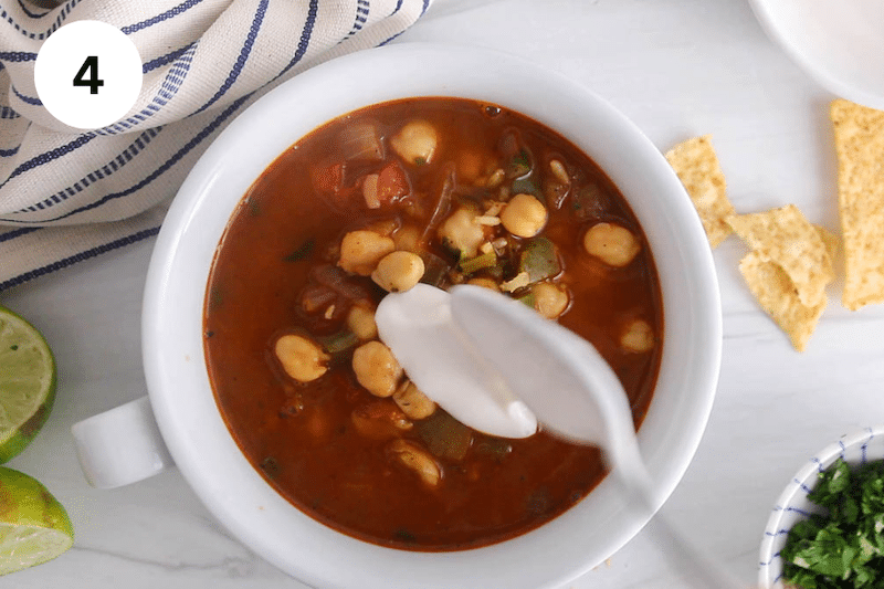 A bowl of soup with a spoon adding vegan sour cream over.