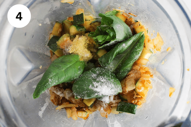 View inside a blender with cooked vegetable and basil.