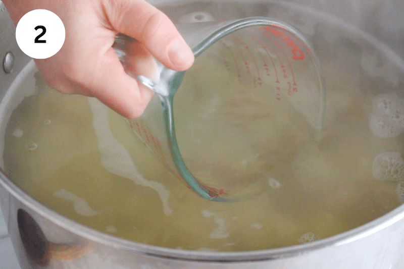 A jar taking some pasta cooking water from a large pot.