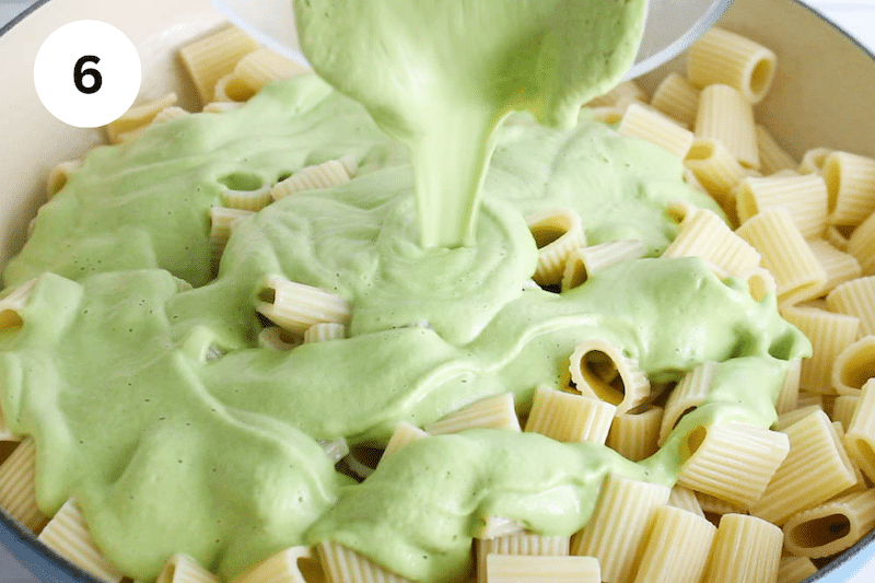 A green sauce pouring over cooked pasta.