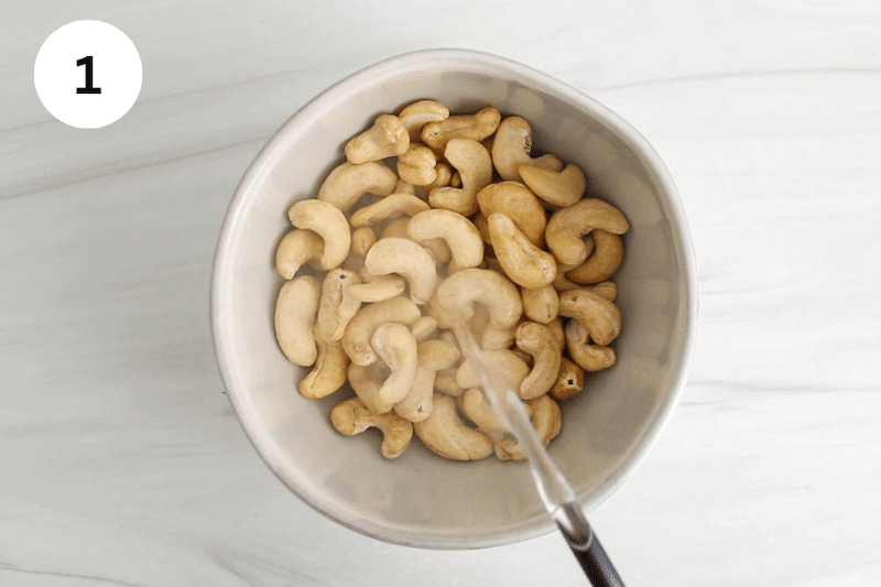 Boiling water pouring over a small bowl with raw cashews.