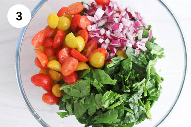 A glass bowl with chopped veggies such as tomatoes, red onion and baby spinach.