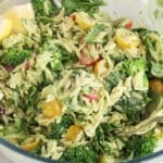 A spoon stirring a pesto orzo pasta salad in a large glass bowl.